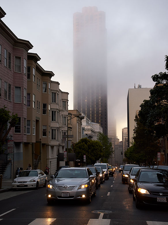 San Francisco street during rush hour with cars lined up and fog shrouding tall buildings at dusk