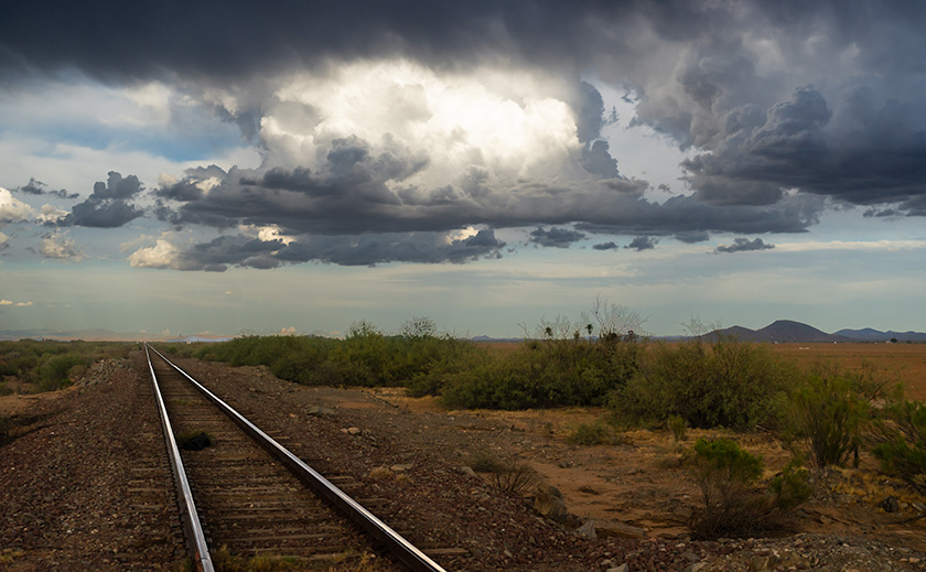 Railroad tracks leading into the stormy horizon under the thunderheads in Aguila, Arizona, capturing the essence of an impending monsoon.