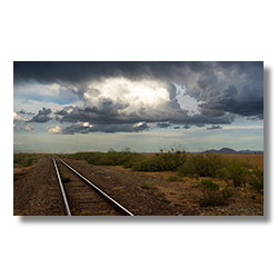 Railroad tracks leading into the stormy horizon under the thunderheads in Aguila, Arizona, capturing the essence of an impending monsoon.