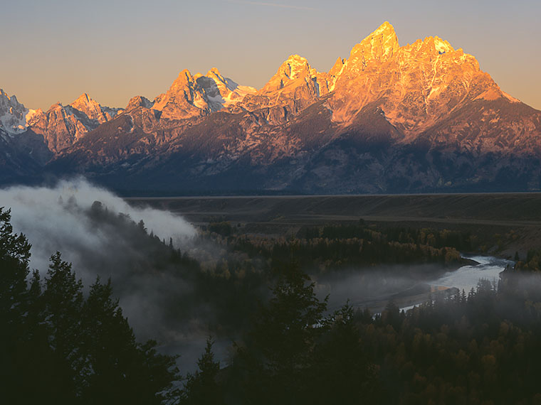 Early morning ground fog tumbles into the Snake River Gorge while the sun comes up on the Grand Teton Mountains.