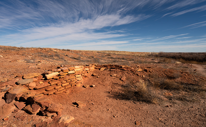 Partial wall of an ancient kiva ruin under a sweeping blue sky in Homolovi State Park, Arizona.