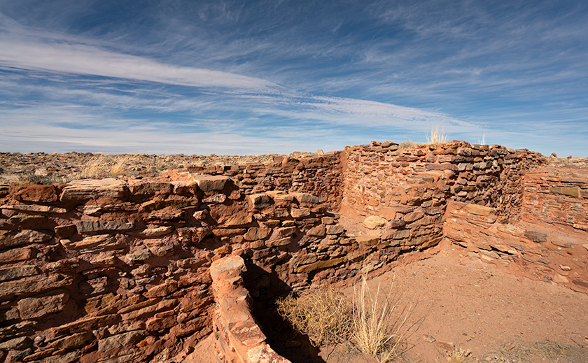 Kiva II ruins at Homolovi State Park under a wide blue sky, remnants of ancient Puebloan culture.