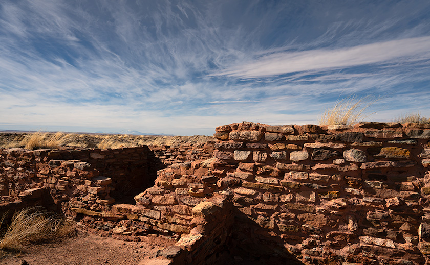 The rugged beauty of Homolovi's Kiva ruins foregrounds the distant San Francisco Peaks under a dynamic Arizona sky.