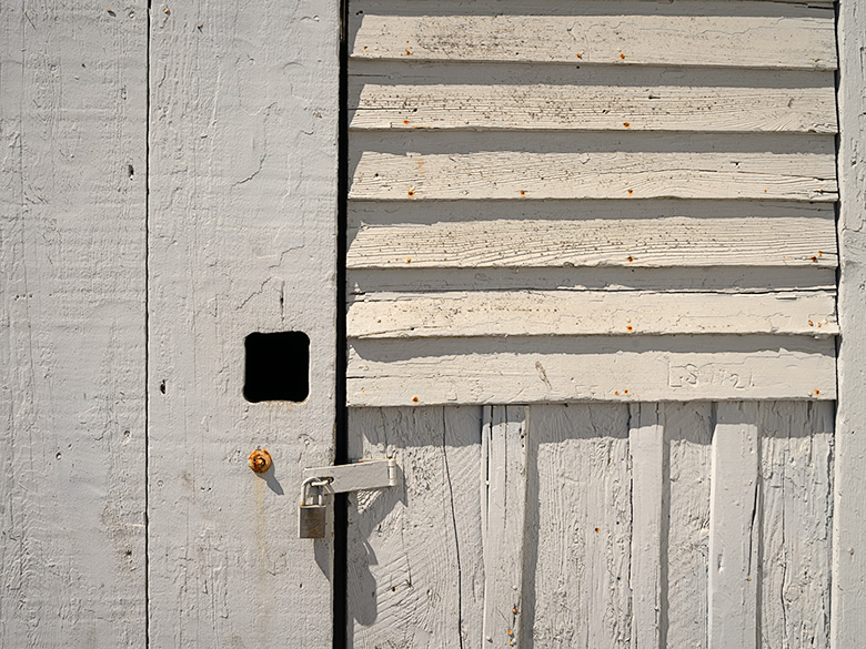 Close-up of a weathered door with a padlock, showing the rustic texture of a building at Pierce Point Ranch, Point Reyes, California