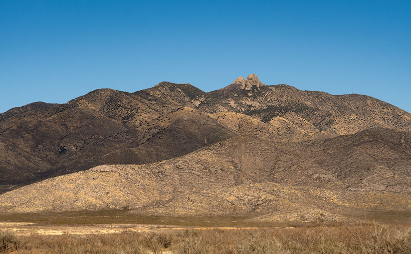View of Dos Cabezas Mountains showing two distinct granite peaks with a backdrop of blue sky and clouds.