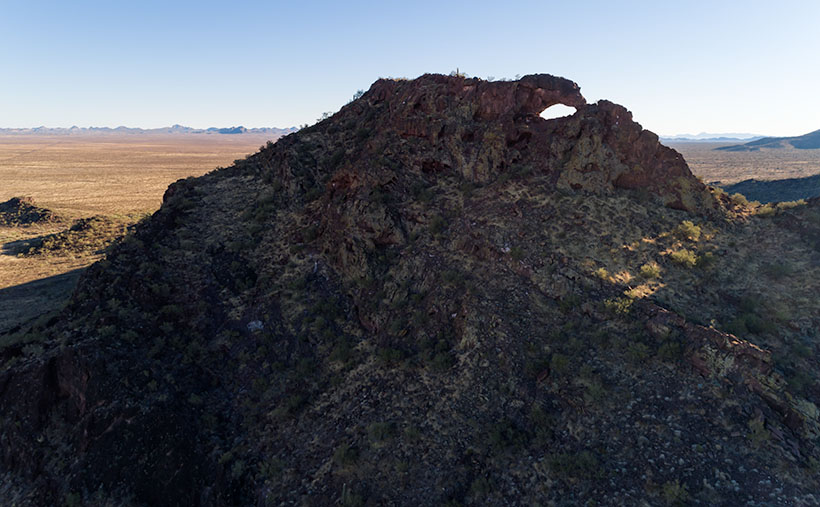 Elevated drone view capturing the natural arch atop Eagle Eye Peak with the Harquahala Plain stretching into the distance.