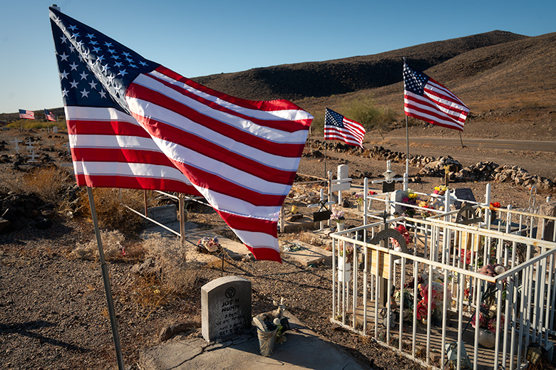 Agua Caliente Pioneer Cemetery with American flags flying over graves on Veterans Day, restored with white crosses for unidentified graves.