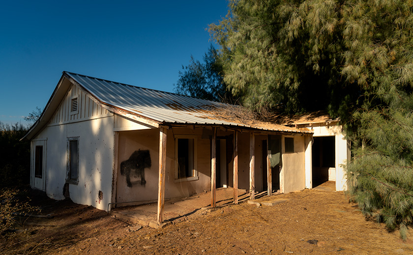 Backside of Palmerita Ranch house with porch and late afternoon sunlight, surrounded by eucalyptus and tamarisk trees.