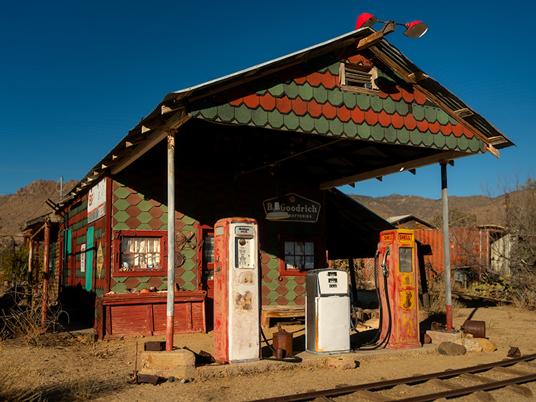 An alpine-style gas station in Chloride, Arizona, with vintage gas pumps, narrow-gauge tracks, and nostalgic yard art under a decorative portico.