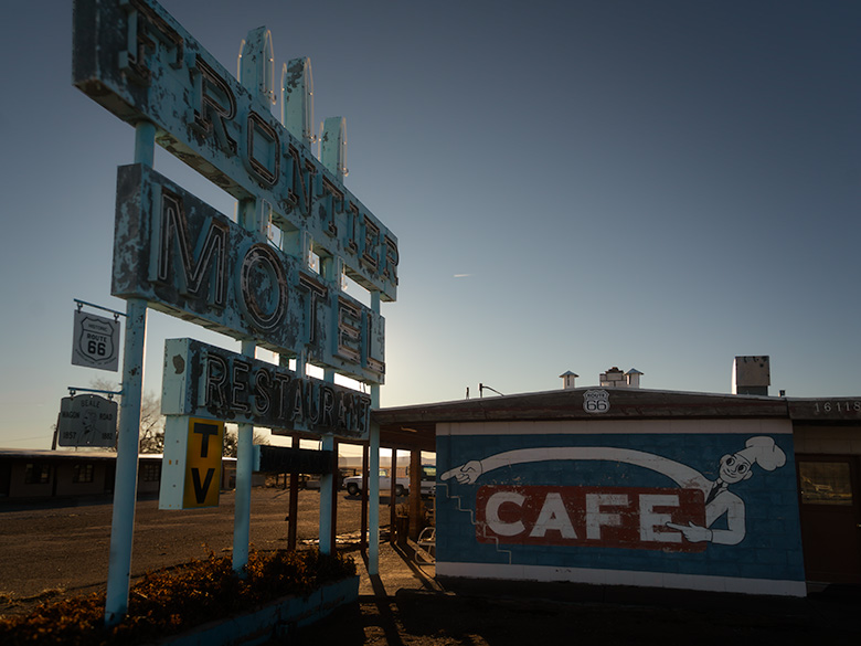 Faded blue Frontier Motel sign with peeling paint and a vintage café mural in Truxton, Arizona, along Route 66.