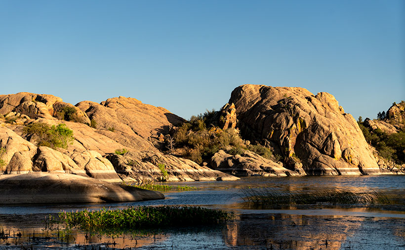 Evening sun illuminating the granite domes over Lake Wilson, contrasting the rugged rocks with the serene ripples of water.