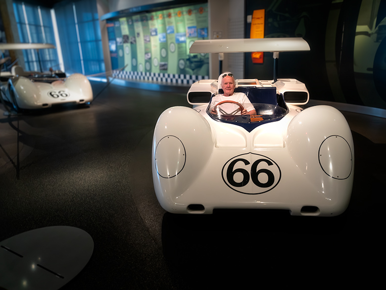 Photographer playfully sitting in a classic display car at an exhibition..