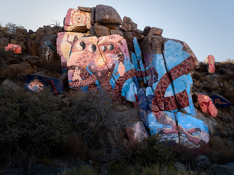 Overview of Roy Purcell’s murals in Chloride, Arizona, showcasing a central cosmic-themed mural surrounded by smaller painted rocks in the Cerbat foothills.