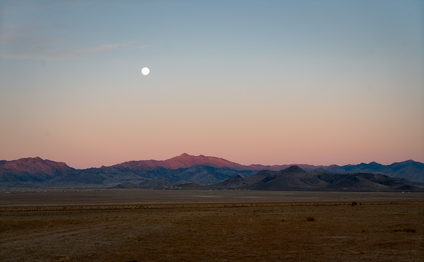 A full moon setting over the Cerbat Mountains at dawn, with pastel desert hues, captured from Route 66 near Kingman, Arizona.