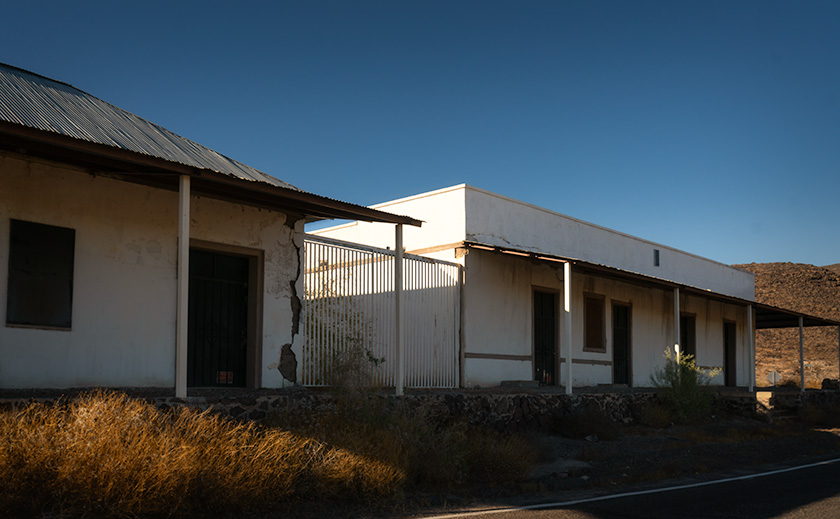 Plaster-covered adobe buildings in Agua Caliente, the former reception and guest quarters of a hot springs resort, with basalt ruins nearby.