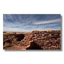 The rugged beauty of Homolovi's Kiva ruins foregrounds the distant San Francisco Peaks under a dynamic Arizona sky.
