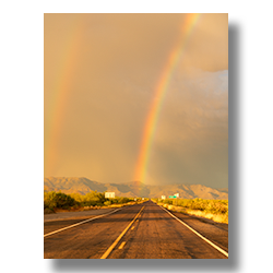 Double rainbows arching over State Route 71 with dark golden clouds and the Weaver Mountains in the background, Congress, Arizona.