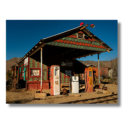 An alpine-style gas station in Chloride, Arizona, with vintage gas pumps, narrow-gauge tracks, and nostalgic yard art under a decorative portico.