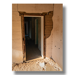 Back door of Palmerita Ranch house with falling plaster revealing adobe block walls.