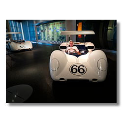 Photographer playfully sitting in a classic display car at an exhibition.