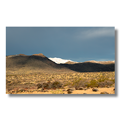 Snow-covered unnamed peak in the Date Creek Range, contrasting with dark storm clouds and the desert landscape