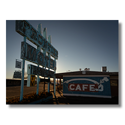 Faded blue Frontier Motel sign with peeling paint and a vintage café mural in Truxton, Arizona, along Route 66.