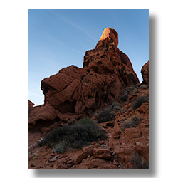 A towering red sandstone formation illuminated by the golden light of the sun, set against the clear blue sky in Valley of Fire State Park, Nevada.
