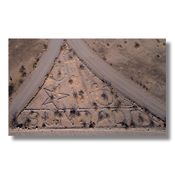 Aerial photo of triangular rock art near Sundad, Arizona, featuring an anchor, star, circles, and the word 'SUNDAD' spelled in stones