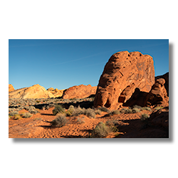 A towering red sandstone rock formation standing prominently against a clear blue sky in the Valley of Fire State Park, Nevada.
