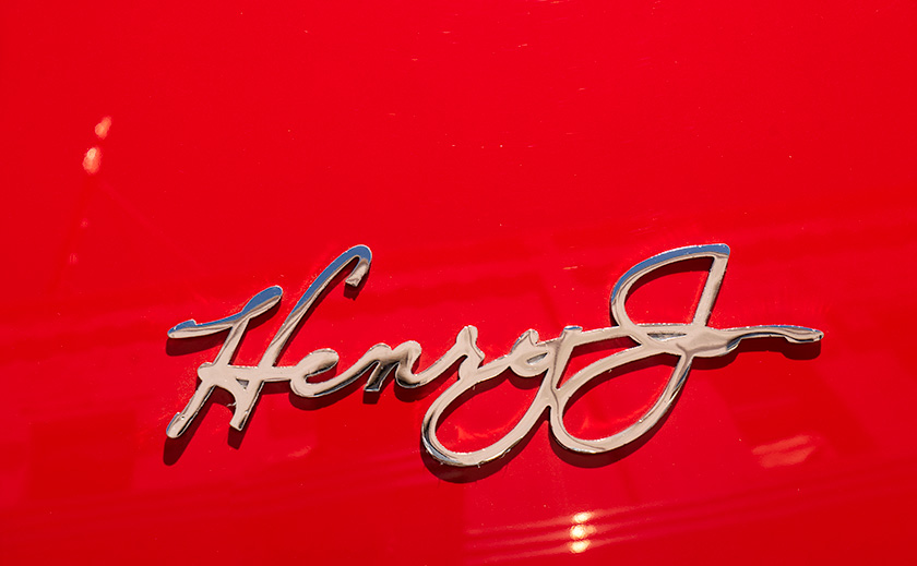 The chrome badge on a bright red Henry J on display at a car show in Kingman, Arizona